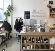 two people sitting at tables in a coffee shop with lots of bottles on the counter