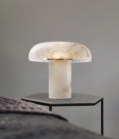 a table lamp sitting on top of a black stand next to a gray wall and bed