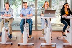 three people sitting at desks with laptops on their laps and one standing up