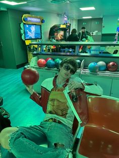 a young man sitting in a chair with an apple on his hand and bowling balls behind him