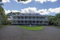 a large white house sitting in the middle of a lush green field next to palm trees