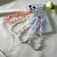 three necklaces are laying on top of a white surface next to a flower and cell phone