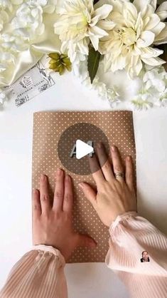 two hands on top of a piece of brown paper with white flowers in the background