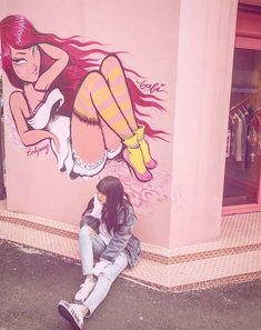 a woman sitting on the ground in front of a pink building with a mural painted on it