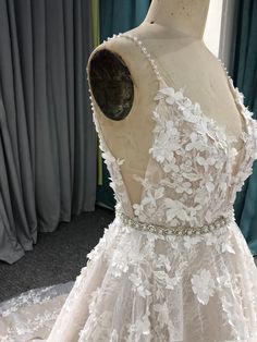 the back of a wedding dress on display in front of a window with blue curtains