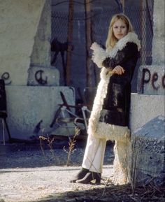 a woman standing in front of a building wearing a long coat with fur on it