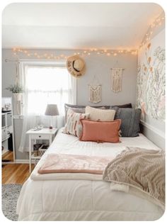 a white bed topped with lots of pillows next to a window covered in string lights