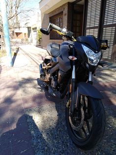 the motorcycle is parked on the side of the road near the building and tree in front of it