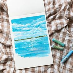 a card with watercolors and crayons next to it on a bed