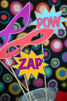 there are some paper masks on sticks in a glass vase with the words pow and zap