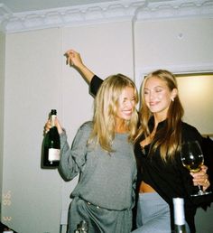 two beautiful women standing next to each other holding wine bottles and glasses in their hands