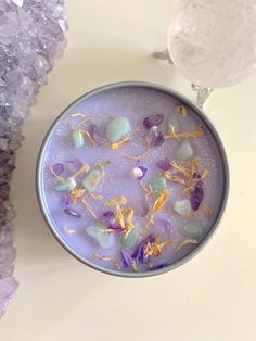 a bowl filled with purple and yellow flowers next to crystal rocks on a white surface