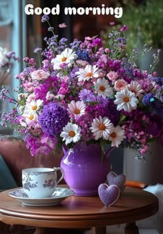 a vase filled with purple and white flowers on top of a table next to a cup