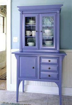 a purple china cabinet with glass doors and drawers in a blue dining room, next to a white wall