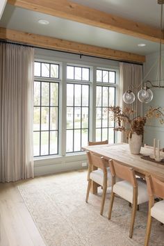 the dining room table is surrounded by chairs and vases with flowers in them, along with two large windows