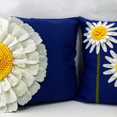 two decorative pillows with white and yellow flowers on them, one has a blue background