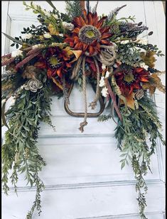 a wreath hanging on the front door with flowers and greenery around it's edges