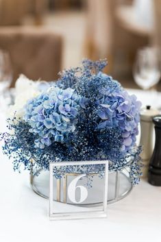 there is a vase with blue flowers in it on top of a white table cloth