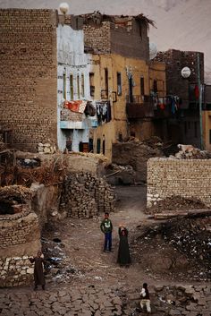 two people standing in the middle of an old town with stone walls and brick buildings