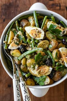 a white bowl filled with green beans, potatoes and other vegetables on top of a wooden table