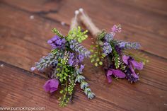 two purple flowers sitting on top of a wooden floor next to a stick with green leaves