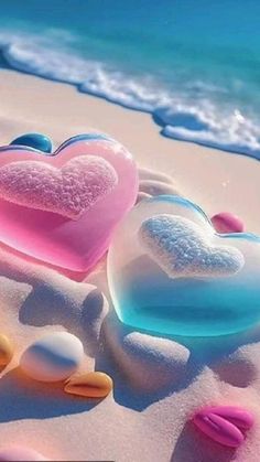 two heart shaped soaps sitting on top of a sandy beach next to the ocean