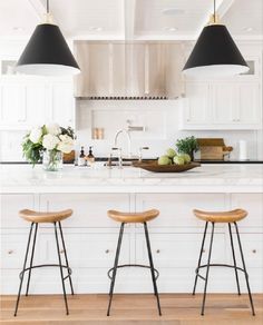 two stools in front of a kitchen island with white cabinets and black pendant lights