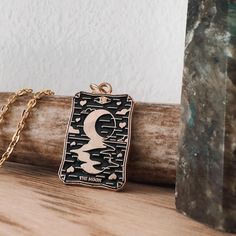 a gold necklace with a black and white design on it sitting on top of a piece of wood