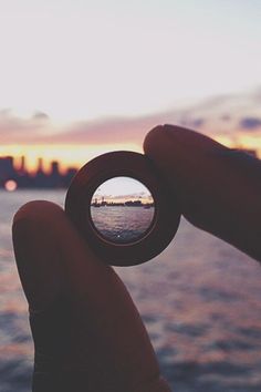 a person holding up a small object in front of the water with buildings in the background