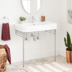 a white sink sitting under a mirror next to a potted plant and towel rack