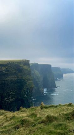 two sheep standing on the edge of a cliff overlooking the ocean with cliffs in the background