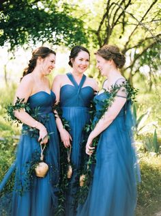 three bridesmaids in blue dresses with greenery around their waist and neckline