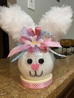 a white ball with feathers and a pink bow on it's head sitting on a counter