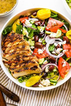 a salad with grilled chicken, tomatoes, cucumber, onions and olives