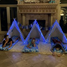 three children laying on pillows in front of a fire place with blue lights around them