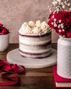 a cake with white frosting and red flowers in vases on a wooden table