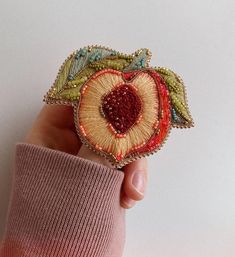 a hand holding an embroidered brooch in the shape of a heart