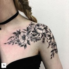 a woman's shoulder with flowers and leaves tattoo on her upper arm, in black ink