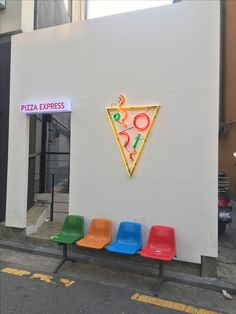 colorful chairs are lined up in front of a wall with a pizza sign on it