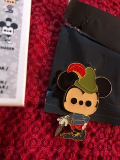 a mickey mouse pin sitting on top of a red carpet next to a black bag