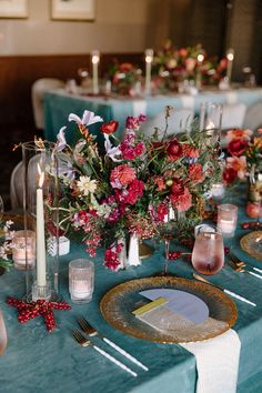 the table is set with candles, plates and flowers on it for a festive dinner