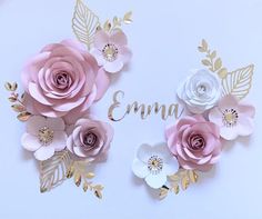 pink and white paper flowers with the word ema in gold lettering on a light blue background