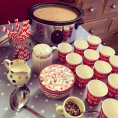 a table topped with cups and bowls filled with marshmallows next to a crock pot