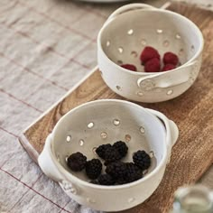 two white bowls filled with raspberries on top of a wooden cutting board