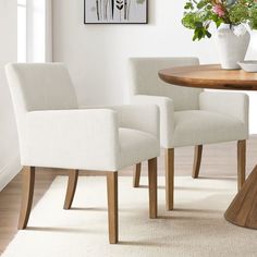 two white chairs sitting in front of a wooden table with flowers on top of it