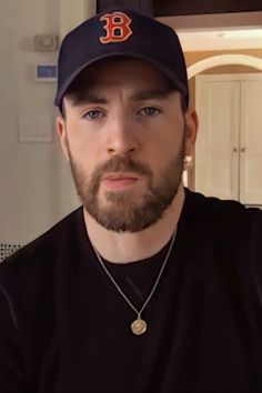 a man with a beard wearing a baseball cap and black shirt is looking at the camera