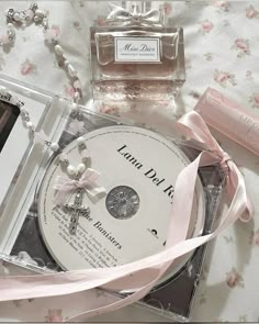 the contents of a perfume bottle, necklace and cd on a bed with pink ribbon