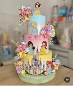 a three tiered cake decorated with princess figurines and flowers on a table