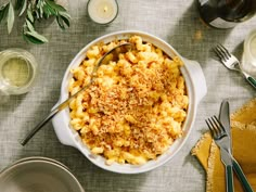 a white bowl filled with macaroni and cheese on top of a table next to silverware