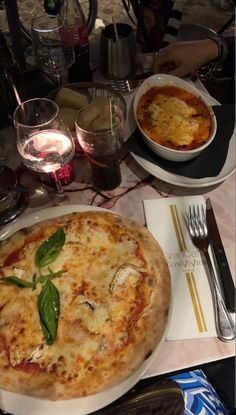 a pizza on a plate next to a glass of wine and silverware at a table